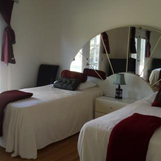 A cozy bedroom with twin beds featuring white bedding and red accents, complemented by a mirror and nightstand with a lamp.