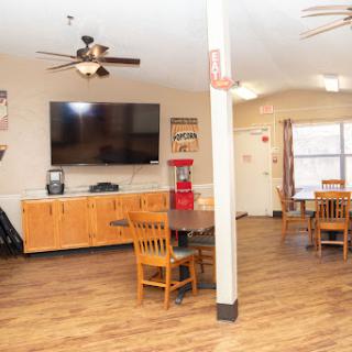 A cozy lounge area featuring wooden furniture, a large television, and ceiling fans.
