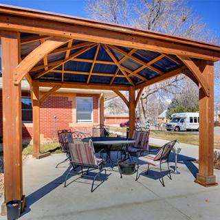 A wooden pergola with a dining set underneath, providing a shaded seating area in a backyard.