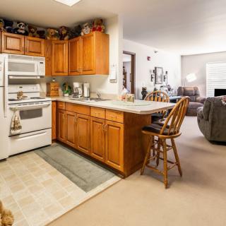 A cozy open-plan kitchen and living room with wooden cabinets and bar stools.