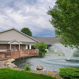 A serene view of a building with a pond and fountain surrounded by lush landscaping.