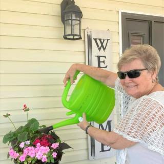 A woman smiles while watering her plants with a green watering can.