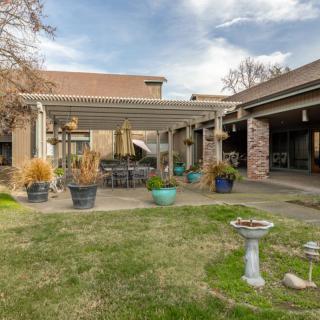 A cozy backyard patio with a pergola, surrounded by potted plants and outdoor seating.