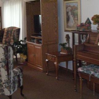 A cozy living room featuring a piano, patterned chair, and a television.