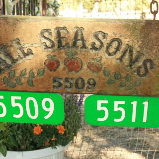A garden sign displaying 'ALL SEASONS' with addresses 5509 and 5511.