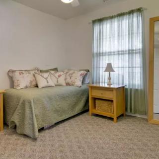 A cozy bedroom with a daybed, nightstand, and a lamp by the window.