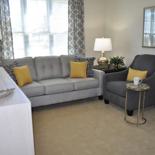 A cozy living room with a gray sofa, armchair, and yellow accent pillows.