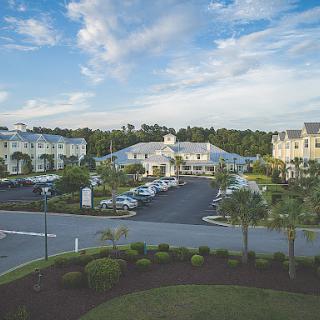 A serene view of a modern building complex surrounded by lush greenery and a clear blue sky.