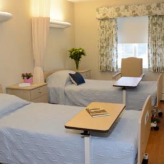 A clean and organized hospital room featuring two beds with overbed tables.