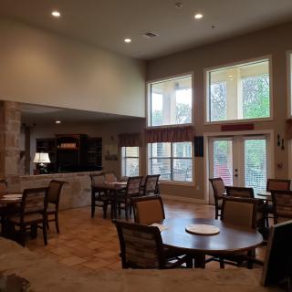 A spacious and cozy dining area with tables and chairs, well-lit by large windows.