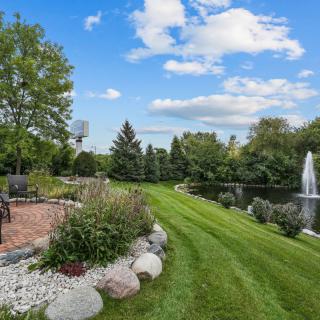 A tranquil garden with a well-manicured lawn, a pathway, and a pond with a fountain.