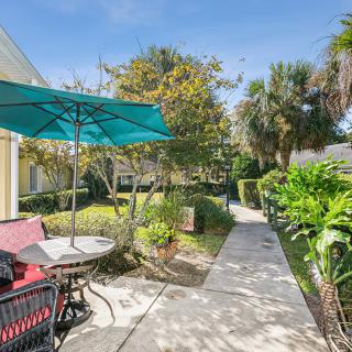 A sunny outdoor patio with a blue umbrella, surrounded by a well-maintained garden and pathway.