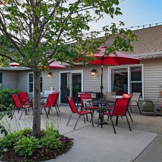 A cozy outdoor patio area with red chairs and umbrellas, surrounded by plants and trees.