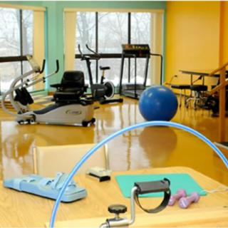 A brightly colored fitness room equipped with exercise machines and physical therapy tools.