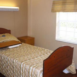 A simple bedroom with a single bed, nightstand, and window.