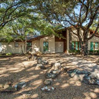 A charming house surrounded by trees with a stone exterior and a spacious front yard.