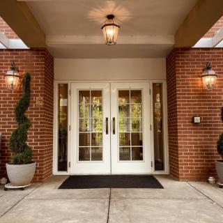 A welcoming entrance with double glass doors set in a brick building, adorned with decorative plants and warm lighting.