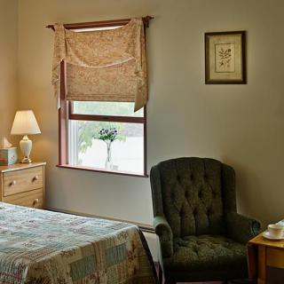 Cozy bedroom with a window view, featuring a patterned bedspread and a comfortable armchair.