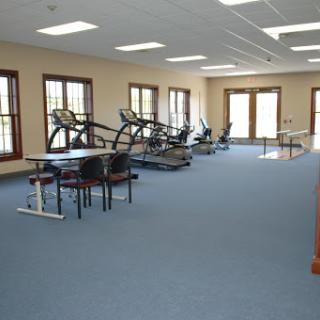 A spacious gym area equipped with exercise machines and tables, featuring large windows for natural light.