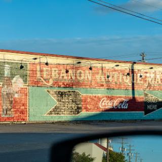 A weathered mural featuring vintage advertisements, including Coca-Cola, on the side of a building in Lebanon.