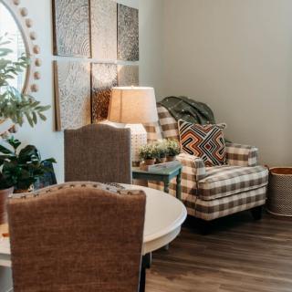 A cozy living room corner with an armchair, decorative pillows, a lamp, and indoor plants.