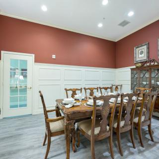An elegant dining room featuring a large wooden table surrounded by matching chairs, set against a warm wall with classic decor.