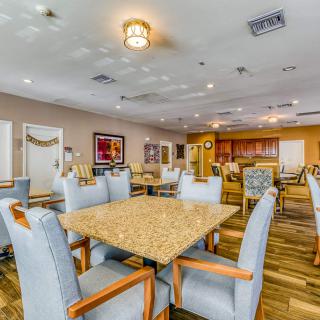 A modern dining room with multiple tables and chairs, featuring wooden floors and ceiling lights.
