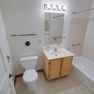A clean and simple bathroom with a toilet, sink, mirror, and bathtub.