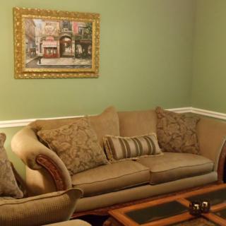 A cozy living room with a beige sofa, patterned cushions, and wall art on green-painted walls.