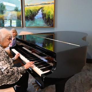 An elderly woman plays a piano while a child observes, showcasing a beautiful moment of intergenerational connection through music.