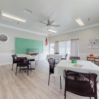 A spacious and well-lit classroom setup, featuring a green chalkboard and arranged tables and chairs.