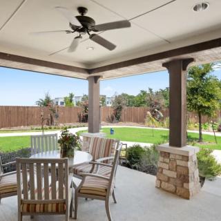 A serene backyard patio with seating area and ceiling fan overlooking a well-maintained garden and lawn.