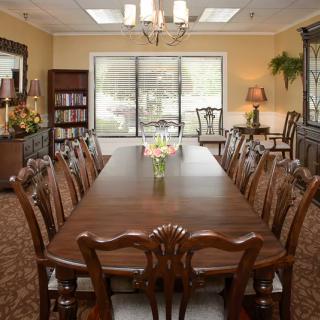 A spacious dining room with a large wooden table surrounded by chairs, featuring floral arrangements and a chandelier.