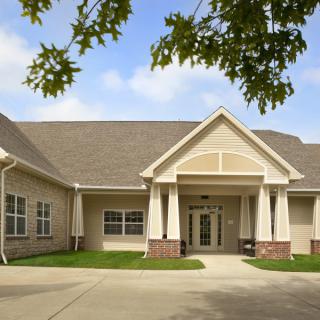 A residential building with a driveway and tree-covered entrance.