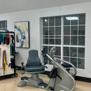 A room with gym equipment including a stationary bike, adjacent to large windows and decorated with colorful artwork.