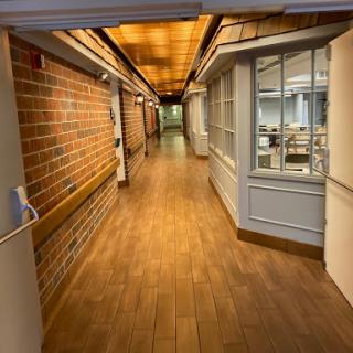 A well-lit corridor featuring brick walls and wooden flooring, leading to office spaces.