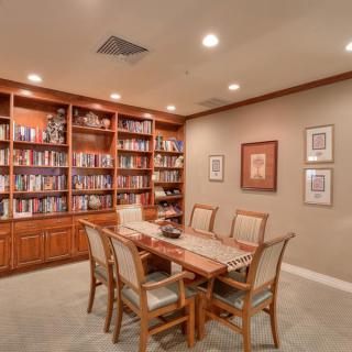 A cozy library room with wooden bookshelves filled with books, a long table, and chairs.