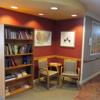 A cozy reading nook with a bookshelf, armchairs, and a small table, adorned with artwork on the walls.
