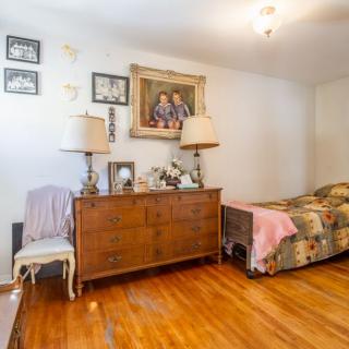 A cozy bedroom featuring a wooden dresser with two lamps and wall art, alongside a single bed with a colorful quilt on a hardwood floor.