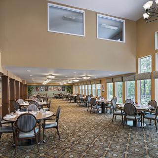 A spacious dining area with neatly arranged tables and chairs, featuring large windows providing natural light.