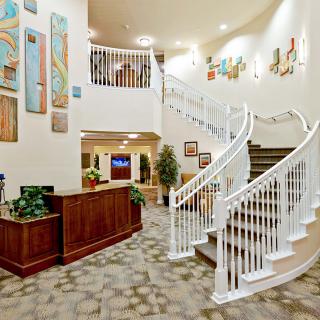 A warmly lit lobby featuring a curved staircase, decorative art, and a reception desk.