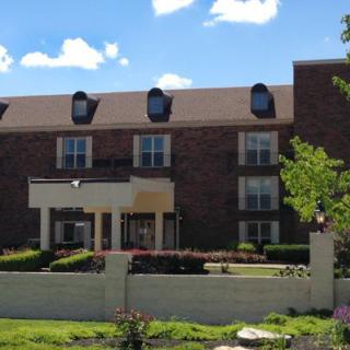 A three-story brick residential building with a landscaped front garden under a clear sky.