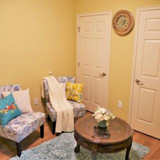 A cozy living room corner with patterned chairs, a round table, and vibrant decor set against yellow walls.