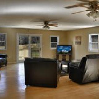 A spacious living room with black leather sofas, a TV, and ceiling fans.