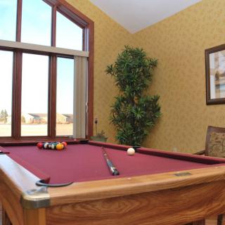 A cozy recreation room featuring a red pool table near a large window, with a cue stick and balls arranged on the table.