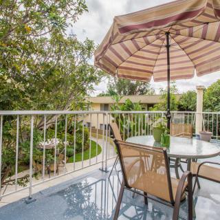 A serene balcony with a patio set, featuring an umbrella and a view of lush greenery.