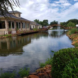 A serene view of a bridge and buildings alongside a lake under a cloudy sky.
