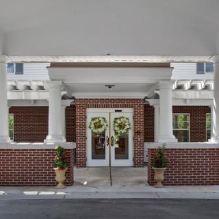 Front entrance of a building featuring double doors with wreaths, columns, and brick walls.