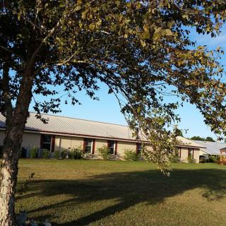 A building surrounded by a grassy yard and trees under a clear blue sky.