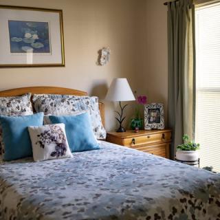 A cozy bedroom with a neatly made bed, colorful pillows, and a wooden nightstand beside the window.